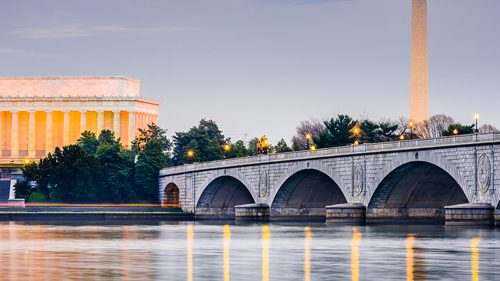 The US Capital building at dusk lit up overlooking a river and bridge